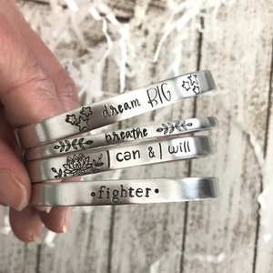 May include: Five silver bracelets with inspirational messages engraved on them. The bracelets read "dream big", "breathe", "I can & I will", and "fighter".