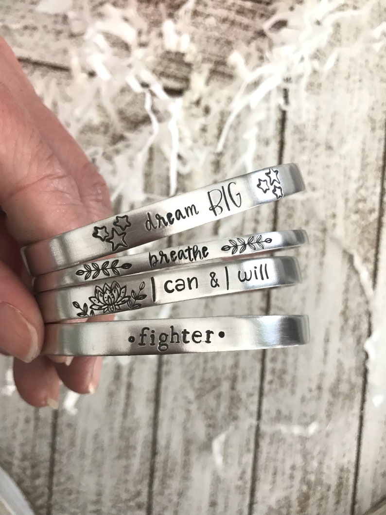 May include: Five silver bracelets with inspirational messages engraved on them. The bracelets read "dream big", "breathe", "I can & I will", and "fighter".