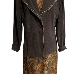 Pode incluir: Um blazer castanho escuro com fecho de um botão e detalhes de costura em cor clara ao longo das lapelas, usado sobre um vestido sem mangas com padrão de leopardo em tons bege e castanho, detalhes florais laranja e textura plissada.