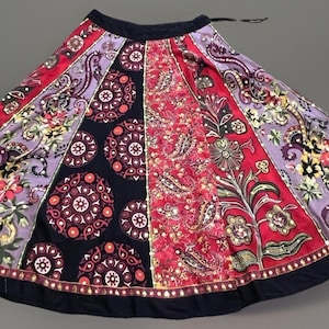 May include: A flared skirt featuring a patchwork design with alternating panels of black, red, and lavender fabric. The panels are decorated with intricate floral, paisley, and circular geometric patterns, finished with a solid black waistband and hem.