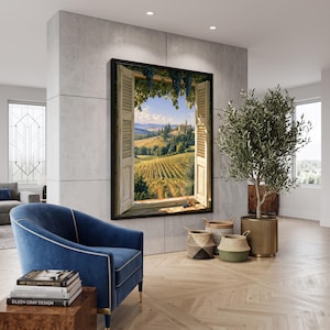 May include: A large rectangular wall art print featuring an open window view of a sunlit vineyard landscape with rolling hills and a stone building. The artwork is framed in black and mounted on a light gray wall above a blue velvet armchair.