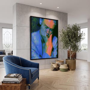 May include: A large rectangular wall art piece featuring a portrait of a person resting their head on their hand, rendered in vibrant neon blue, green, and orange hues with a digital glitch effect, framed in a thin black border on a concrete wall.