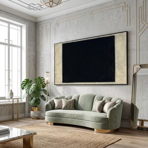 May include: A large rectangular wall art piece featuring a solid black center block framed by a light beige border, displayed in a horizontal orientation. The artwork is mounted on a wall above a curved light green sofa with gold base accents.