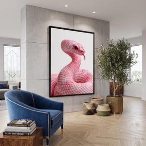 May include: A large rectangular wall art piece featuring a high-resolution photograph of a bright pink snake with a visible red tongue, set against a plain white background and enclosed in a thin black frame, displayed on a grey concrete wall.