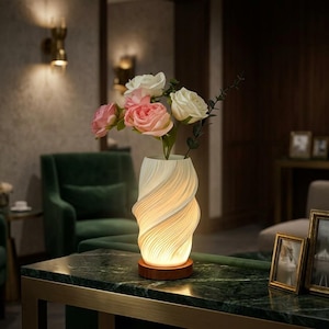 Puede incluir: Una lámpara de jarrón blanca con textura en espiral y un brillo interno cálido, apoyada sobre una base circular de madera. El jarrón contiene un ramo de rosas artificiales rosas y blancas con hojas verdes, creando un suave arreglo floral.