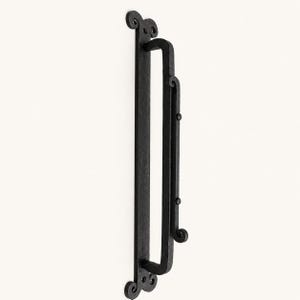 Pode incluir: Um puxador de porta vertical longo em metal preto com acabamento texturizado. O puxador possui uma placa traseira retangular plana com extremidades decorativas enroladas e uma secção de aderência arqueada robusta com dois rebites circulares.