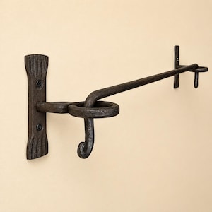 May include: A dark brown, hand-forged metal towel bar featuring a textured, hammered finish. The bar is supported by two vertical wall-mounted brackets with flared ends, each secured by two screws, and includes a decorative hook on the left side.
