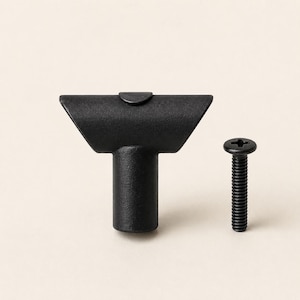 Puede incluir: Un pomo para mueble en forma de T de color negro mate con una base cilíndrica y una barra superior horizontal, acompañado de un tornillo de metal negro a juego con cabeza Phillips para su instalación en muebles o armarios.
