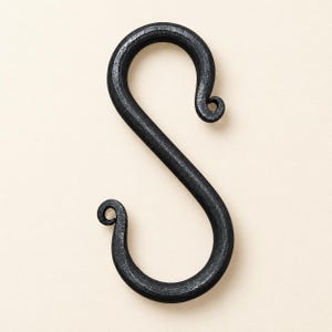 May include: A black metal S-hook with a textured, hand-forged appearance. The hook features a curved, serpentine shape with two tightly coiled, rounded ends that taper slightly, providing a functional design for hanging various household items.