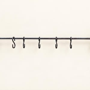 May include: A dark brown metal wall-mounted rack featuring a horizontal rod supported by two decorative brackets at each end. The rack includes six removable S-shaped hooks hanging from the rod for storage and organization purposes.