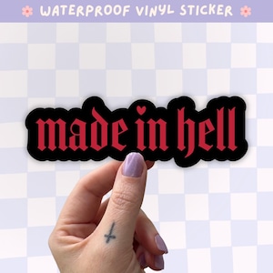 Peut inclure: Un autocollant en vinyle imperméable avec le texte "made in hell" écrit dans une police gothique rouge et audacieuse. Les lettres sont sur un fond noir uni avec une petite icône de cœur rouge placée au-dessus de la lettre i du mot in.