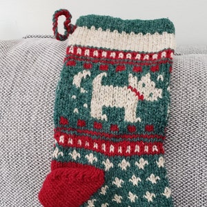 May include: A green and red knitted Christmas stocking with a white dog design. The stocking has a loop at the top for hanging.