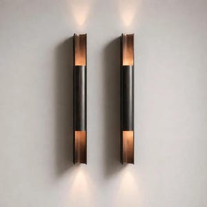 May include: Two vertical wall sconces featuring a dark metallic cylindrical body with open top and bottom sections. Each fixture emits a warm, focused light beam directed both upward and downward, creating a symmetrical illumination pattern.