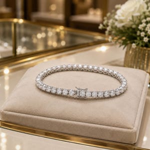 May include: A silver-toned tennis bracelet featuring a continuous row of round, clear, faceted stones set in a metallic frame. The bracelet is secured with a rectangular box clasp mechanism, showcasing a uniform design of sparkling circular links.