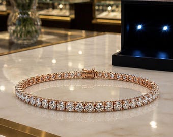 May include: A rose gold tennis bracelet featuring a continuous row of round, brilliant-cut clear stones. The bracelet is designed with a secure metal box clasp mechanism and is laid out in a circular shape on a polished, light-colored surface.