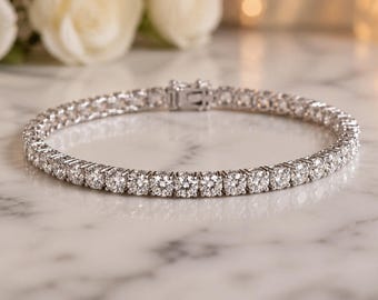 May include: A silver-toned tennis bracelet featuring a continuous row of round, clear, faceted stones set in a metallic frame. The bracelet is circular in shape and includes a secure box clasp mechanism visible at the top of the band.