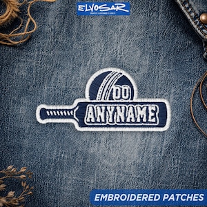 May include: A dark blue embroidered patch shaped like a cricket bat and ball. The patch features a white border and white stitching. The word ANYNAME is embroidered in white capital letters across the center of the bat portion of the patch.