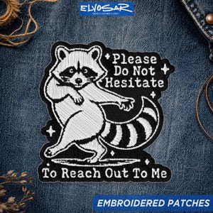 Peut inclure: Un écusson brodé représentant un raton laveur blanc sur fond noir avec le texte Please Do Not Hesitate To Reach Out To Me. Le raton laveur est représenté dans une pose dynamique avec une queue rayée, entouré de petits accents en forme d'étoile.