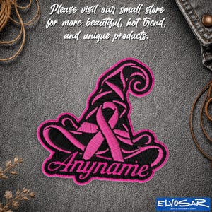 May include: An embroidered patch featuring a black witch hat with a bright pink ribbon wrapped around the center. The word "Anyname" is stitched in pink cursive script at the bottom of the hat. The design has a thick pink border outline.