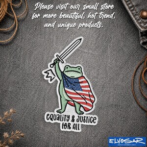 Peut inclure: Un écusson brodé représentant une grenouille verte tenant une épée argentée et portant un drapeau des États-Unis en guise de cape. Le texte "EQUALITY & JUSTICE FOR ALL" est brodé en noir sous la grenouille sur un tissu denim gris foncé.