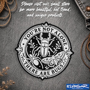 May include: A circular black and white embroidered patch featuring a stag beetle, a spider, and a moth. The text reads "YOU'RE NOT ALONE THERE ARE BUGS" in a circular border. The design includes decorative flourishes and botanical elements.