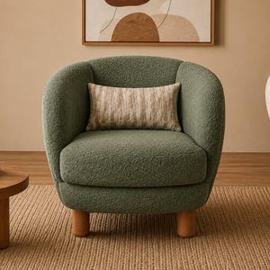 May include: A sage green armchair upholstered in a textured bouclé fabric with a rounded back and seat. The chair features four short, cylindrical light wood legs and includes a rectangular lumbar pillow with a neutral, multi-toned pattern.