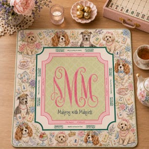 May include: A square mahjong mat featuring a central pink monogram with the text Mahjong with Mahgirls, surrounded by illustrations of dogs wearing floral crowns and pearls, interspersed with mahjong tiles, teapots, and floral patterns.