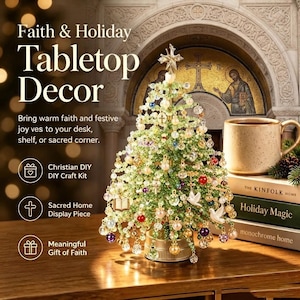 May include: A tabletop Christmas tree decoration crafted from green beads and clear crystals, adorned with small hanging charms including crosses, doves, and books, topped with a star, and set on a gold-toned base, displayed on a wooden surface.