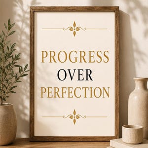 Może przedstawiać: Prostokątna drewniana ramka zawierająca biały wydruk ze złotym napisem PROGRESS i PERFECTION oraz czarnym napisem OVER pośrodku. Projekt zawiera złote ozdobne zawijasy nad i pod tekstem, wyśrodkowane na stronie.