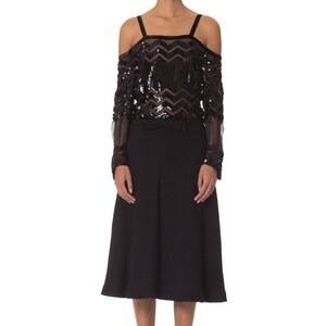 May include: A black off-the-shoulder top with sequin and sheer long sleeves, paired with a black skirt. The top features a chevron pattern and thin straps. The outfit is completed with black platform heels.