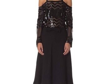 May include: A black off-the-shoulder top with sequin and sheer long sleeves, paired with a black skirt. The top features a chevron pattern and thin straps. The outfit is completed with black platform heels.
