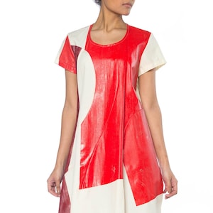 May include: A short-sleeved dress with a bold geometric design. The dress features a color block pattern with red, cream, and burgundy panels. The dress has a round neckline and a loose, A-line silhouette.
