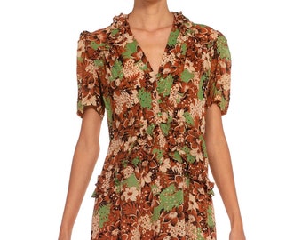 May include: A short-sleeved dress with a floral print in shades of brown, green, and white. The dress has a ruffled collar and a button-up front.