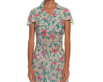 May include: A vintage teal blue dress with a floral print featuring pink and white flowers. The dress has a collared neckline, short sleeves, and a pleated skirt.