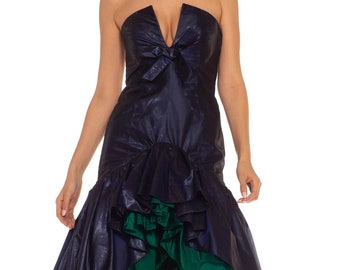 May include: A strapless dress with a deep V-neckline and a bow at the bust. The dress is made of a dark blue fabric with a green ruffled skirt.