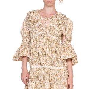 May include: A white floral print dress with a gathered bodice and a tie at the neckline. The dress has 3/4 sleeves with a bell shape and a gathered skirt.