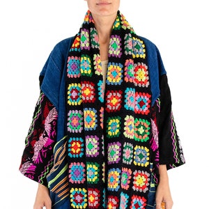 May include: A black denim jacket with colorful crocheted trim. The jacket has a patchwork design with different fabrics and patterns. The crocheted trim is a long scarf that is wrapped around the neck and hangs down the front of the jacket.