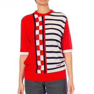 May include: Red and white striped short-sleeved sweater with a checkered pattern on the left side. The sweater has the word "Cacharel" embroidered on the right side.