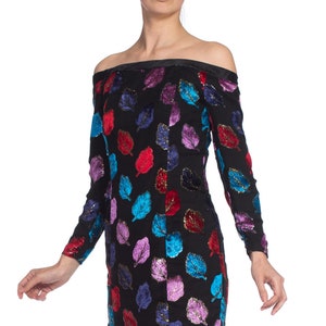 May include: Off-the-shoulder dress with long sleeves, featuring a black background and a colorful leaf pattern. The leaves are made of velvet and have a shiny, iridescent finish.