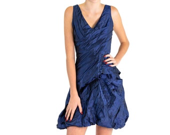 May include: A woman wearing a navy blue sleeveless dress with a ruffled skirt and a V-neckline. She is wearing black heels.
