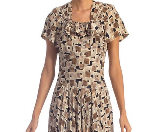 May include: A beige and brown dress with a geometric print and a bow at the neckline. The dress has short sleeves and a knee-length skirt.