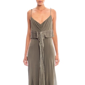 May include: A long, olive green, sleeveless dress with a pleated detail at the waist and a flowing skirt.