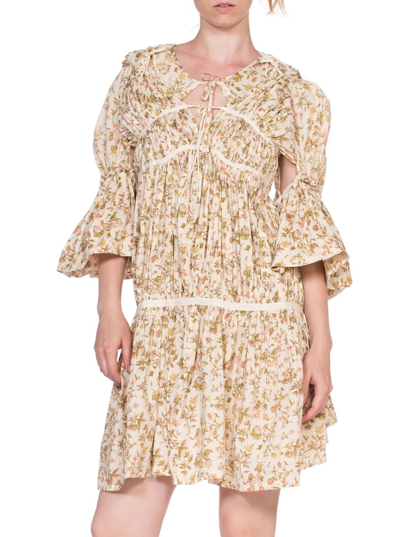 May include: A white floral print dress with a gathered bodice and a tie at the neckline. The dress has 3/4 sleeves with a bell shape and a gathered skirt.