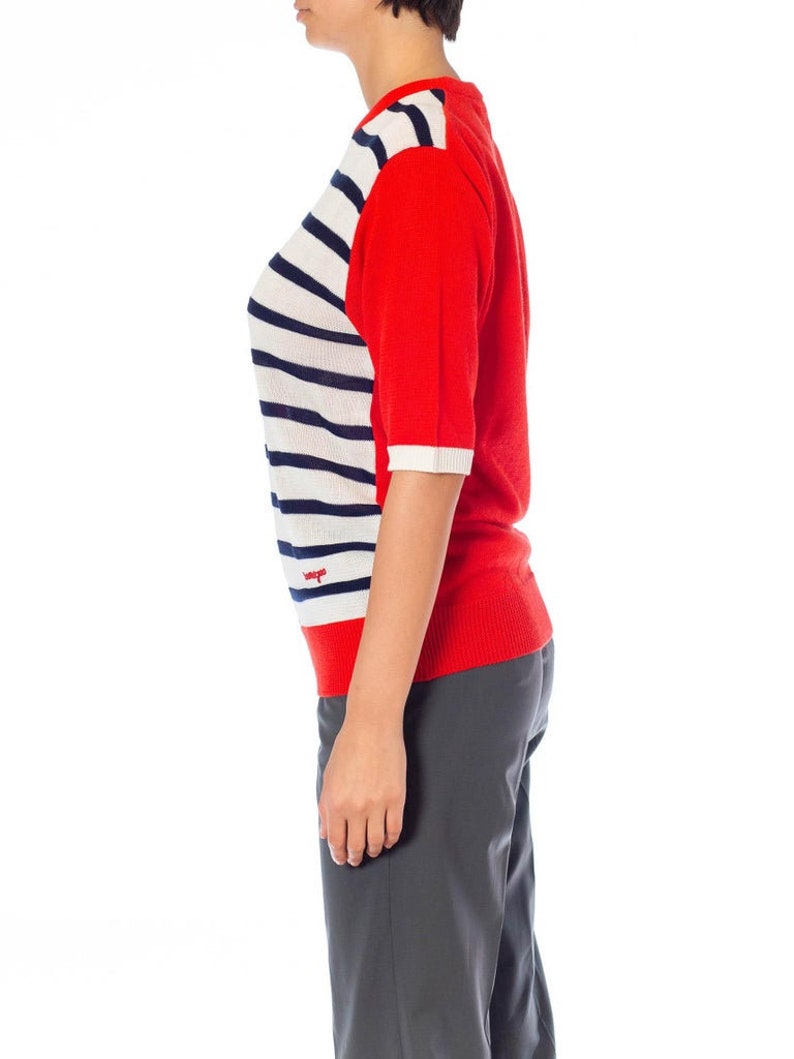 May include: A red and white striped short-sleeved sweater with a red logo on the front. The sweater is made of a soft, comfortable material.