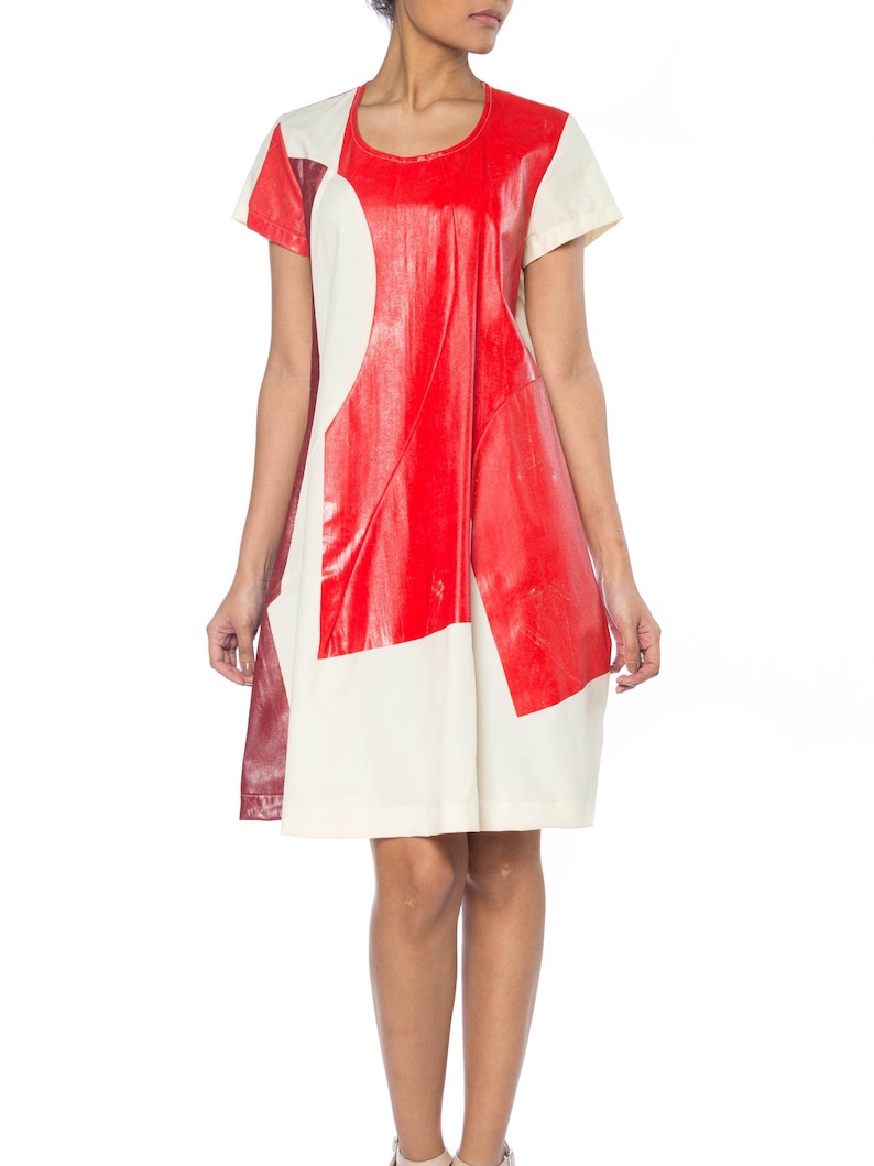 Puede incluir: Vestido de manga corta con un dise&ntilde;o geom&eacute;trico audaz. El vestido presenta un patr&oacute;n de bloques de color con paneles rojos, crema y burdeos. El vestido tiene un cuello redondo y una silueta suelta en forma de A.