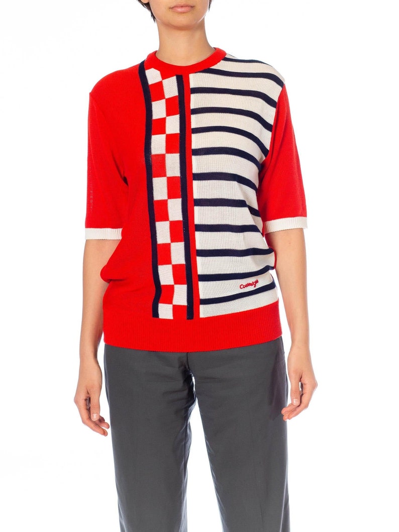 May include: Red and white striped short-sleeved sweater with a checkered pattern on the left side. The sweater has the word "Cacharel" embroidered on the right side.
