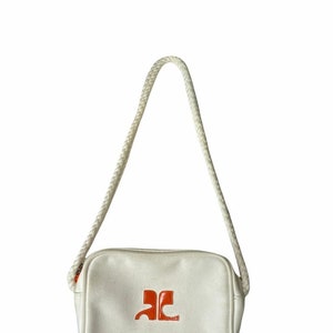 May include: A white canvas crossbody bag with a rope strap and an orange logo.