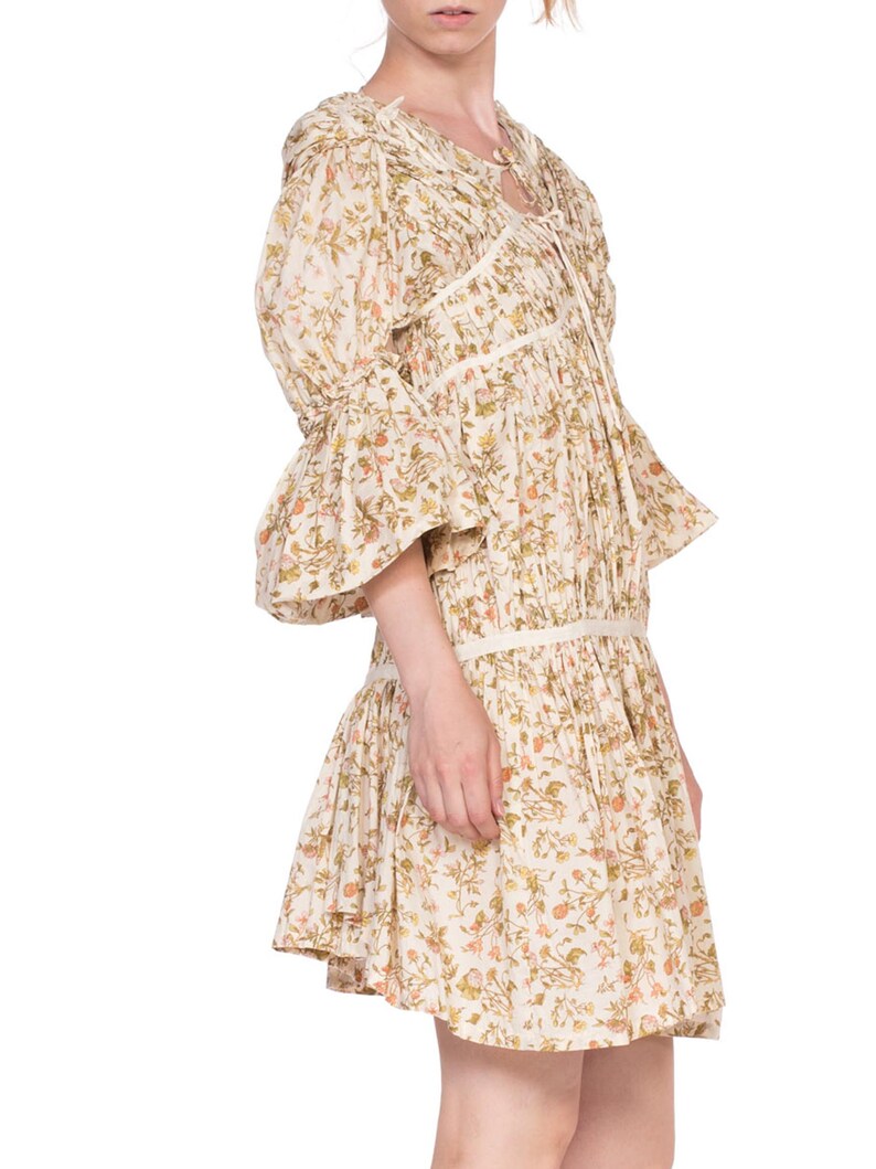 May include: A white dress with a floral print and a tie at the neck. The dress has a ruffled hem and 3/4 sleeves.