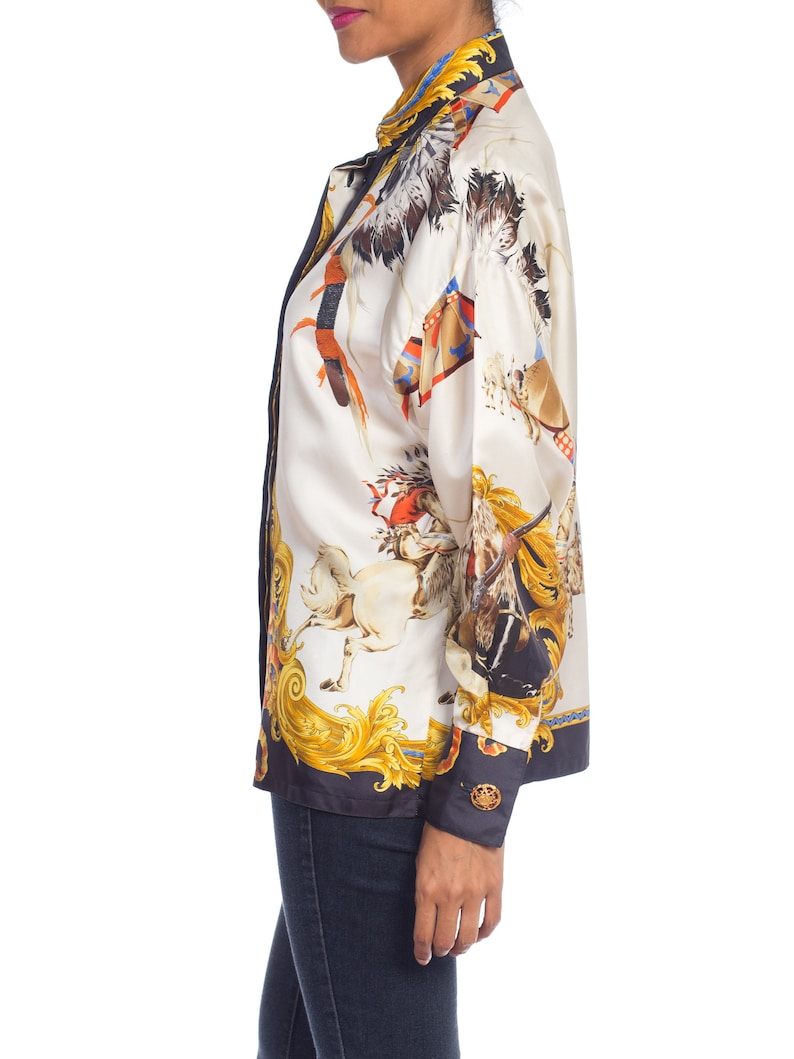May include: A white silk blouse with a colorful print of horses and riders. The print features gold accents and a black background. The blouse has a long sleeve and a button-up front.