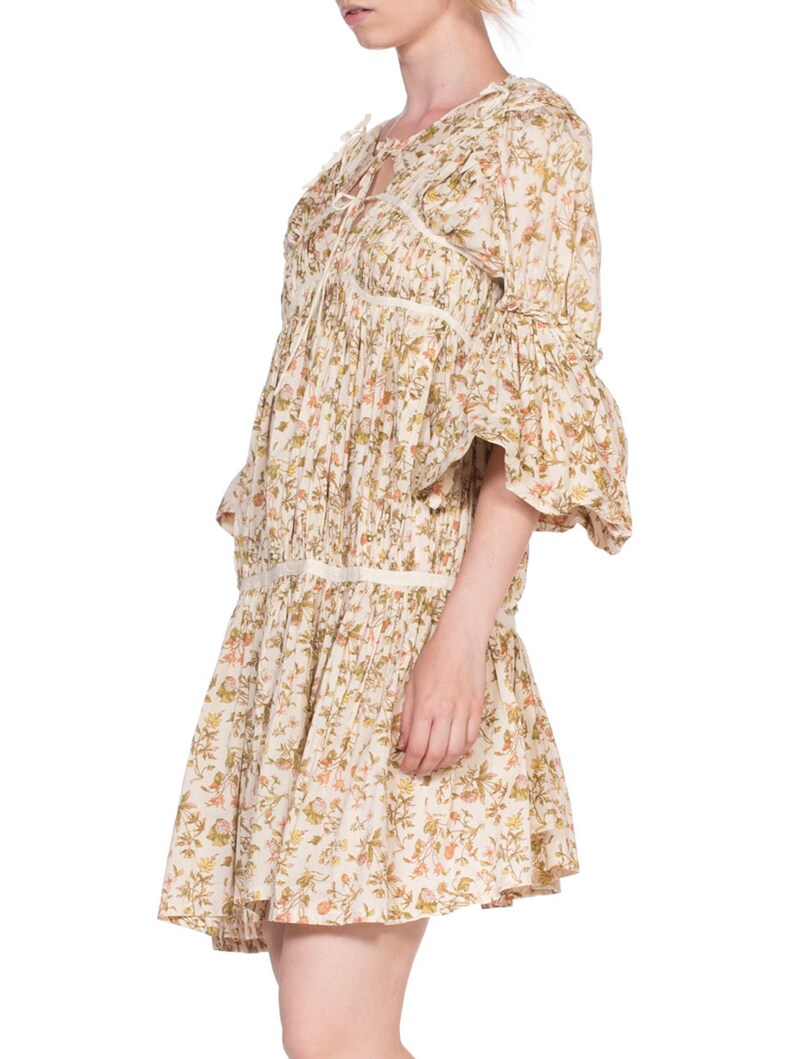 May include: A white floral print mini dress with a tie at the neckline and 3/4 sleeves. The dress has a gathered skirt and a fitted bodice.